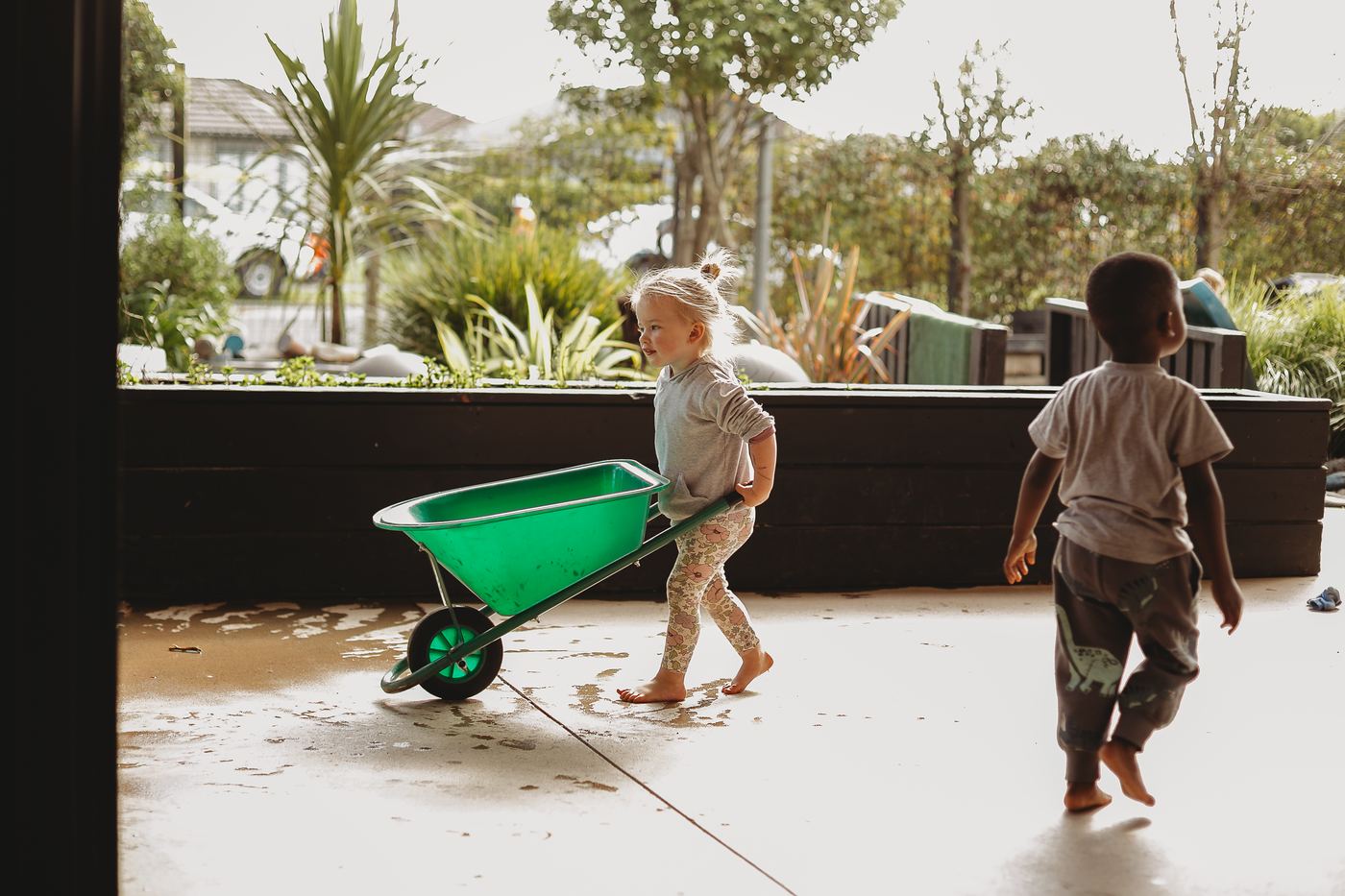 Two children pushing a wheelbarrow across the courtyard